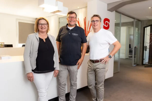 Gruppenfoto in einem modernen Büro, auf dem zwei Mitglieder der Geschäftsführung und unser Kunde von St. Kilian's zu sehen sind. Im Hintergrund ist eine Empfangstheke und eine Büroumgebung zu sehen.