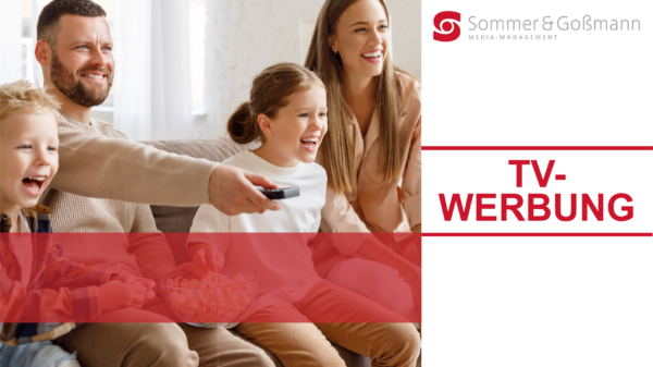 Fröhliche Familie, die zusammen auf einem Sofa sitzt, während der Vater mit der Fernbedienung den Fernseher steuert und die Kinder Popcorn essen.