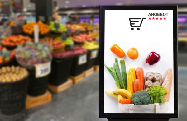 Gemüseabteilung: Im Fokus steht ein Bildschirm auf dem man eine gefüllte Einkauftüte sieht und oben steht Angebot