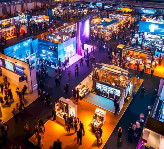 Aerial view of a bustling trade show or exhibition with numerous booths, attendees, and vibrant lighting creating a dynamic atmosphere of commerce and networking